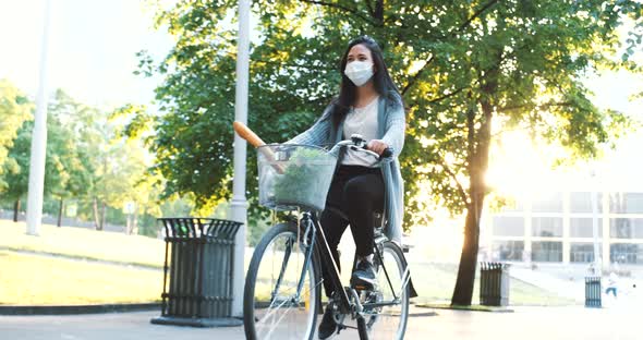 Riding a bicycle in city park with mask. Girl with bike in amazing sunset light. Cycling in city