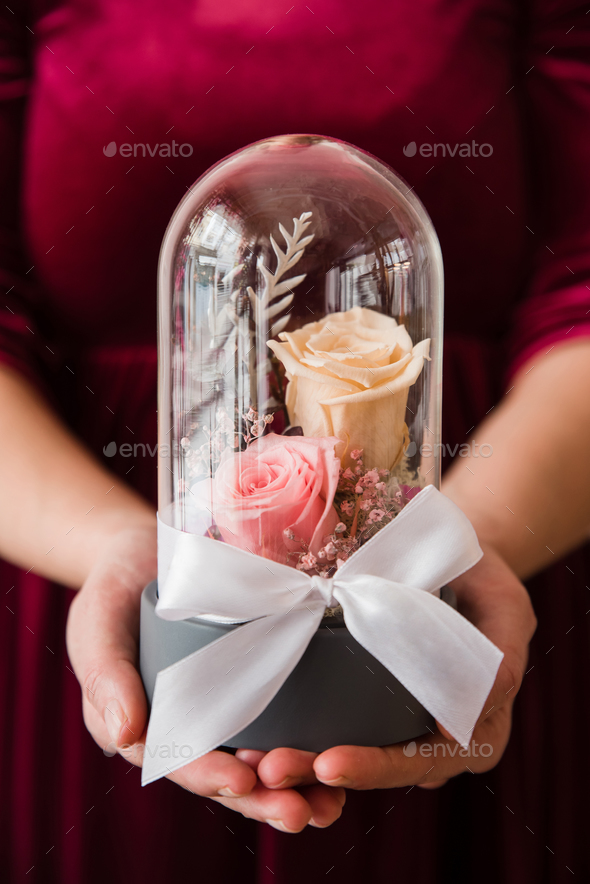 Womans hands holding long-lasting roses in a glass dome