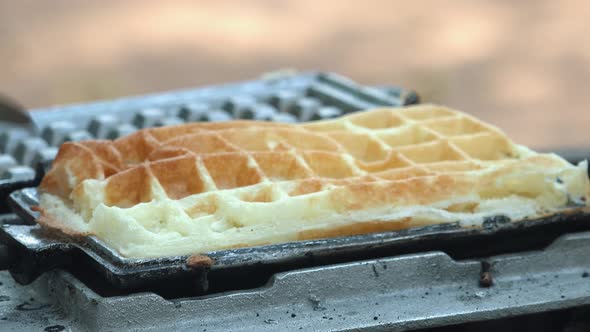 Close Shot of a Waffle Iron Being Opened with the Waffle Being Red with Tongs alt
