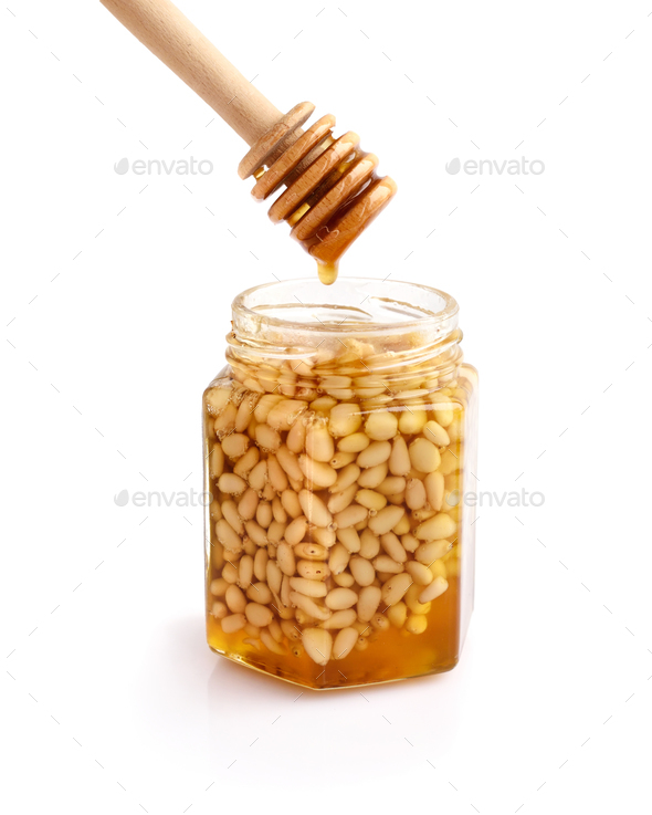 A honey jar with pine nuts and a spoon for honey on white backgr