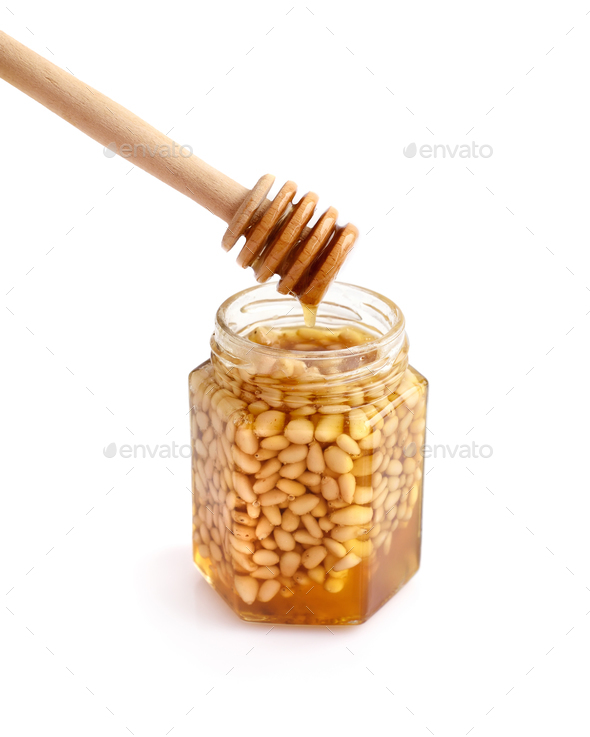 A honey jar with pine nuts and a spoon for honey on white backgr