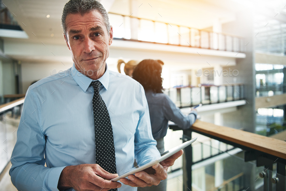 Focused businessman standing with a tablet in an office corridor - Stock Photo - Images