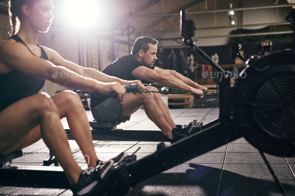Sportsmen doing exercises with rowing machine together