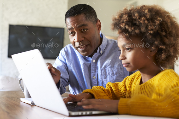 Black girl using a laptop computer sitting at table in the dining room with her home tutor - Stock Photo - Images