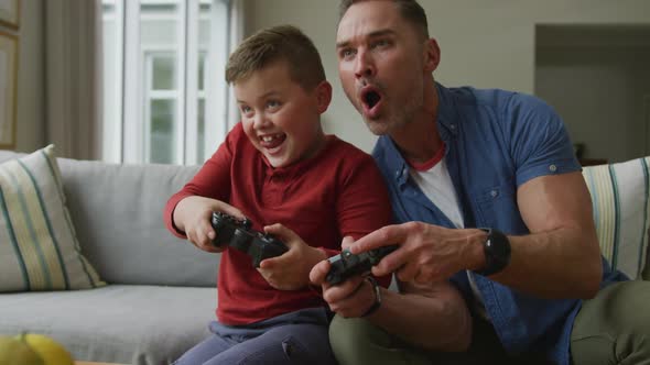 Happy caucasian father with son sitting in living room and playing video games alt