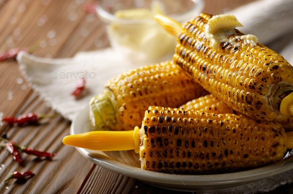 Wooden table with deep grilled sweet corn cobs under melting but