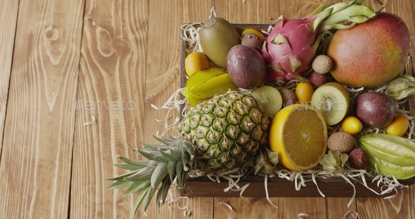 Panoramic video top view on a box with variety fresh natural organic exotic fruits on a wooden