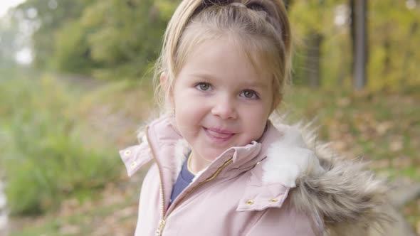 Cute Little Caucasian Girl Looks Around and at the Camera with an Excited Smile in a Park  Closeup alt