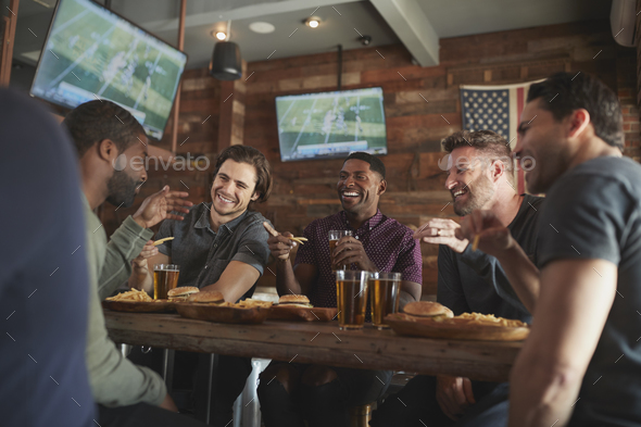 Male Friends Drinking Beer And Eating Burgers In Sports Bar