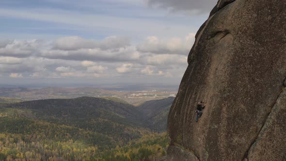 A Young Man Climbs To the Top of a Mountain on a Vertical Wall with a Great View of the Valley