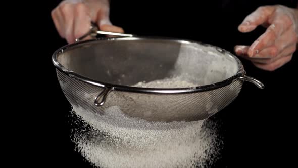 Closeup of White Flour is Falling Through a Steel Sieve on Black Background