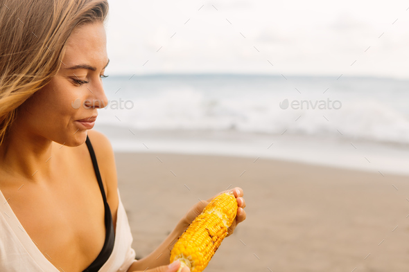 Beautiful vegetarian girl eat corn at seaside.