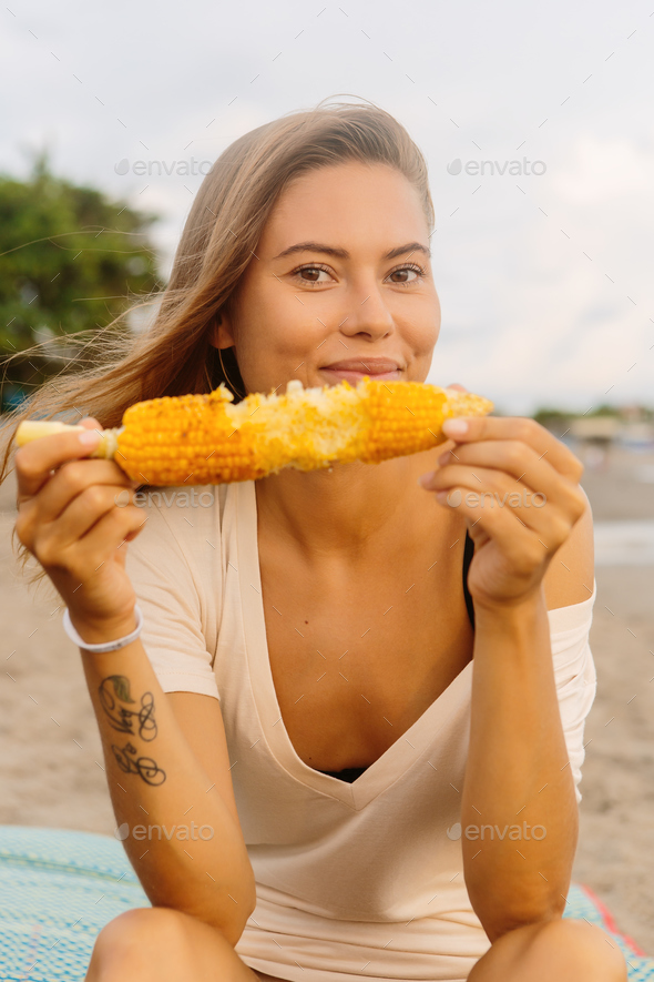Beautiful vegetarian girl eat corn at seaside.