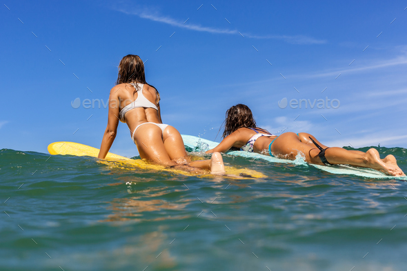 Two beautiful sporty girls surfing in the ocean. - Stock Photo - Images