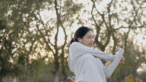 Beautiful Asian woman runner athlete listening music wearing sportswear stretching.