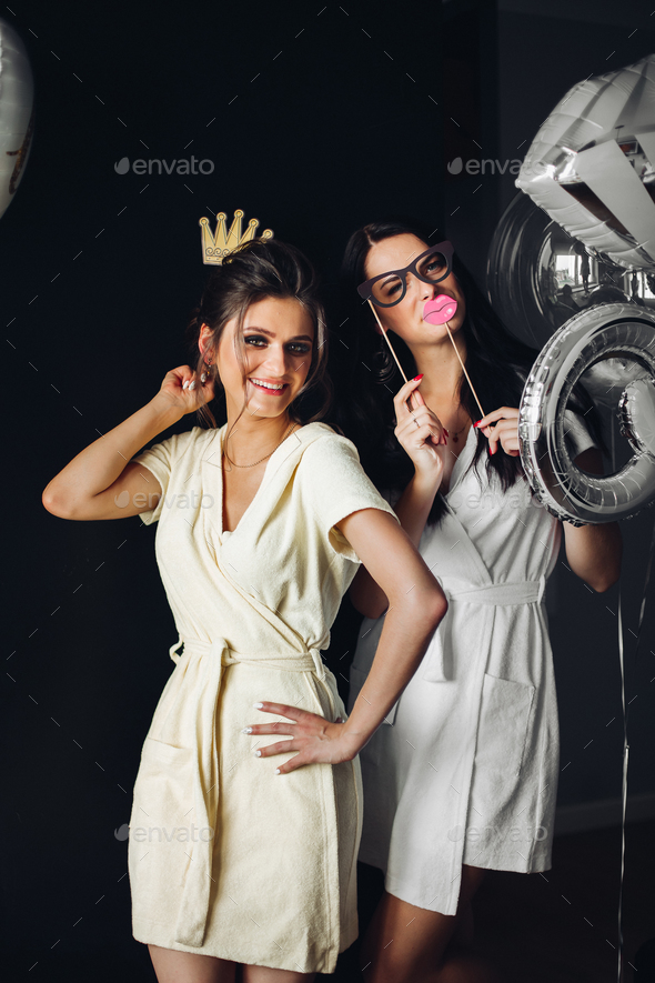 Two young ladies holding accessories and posing at camera - Stock Photo - Images