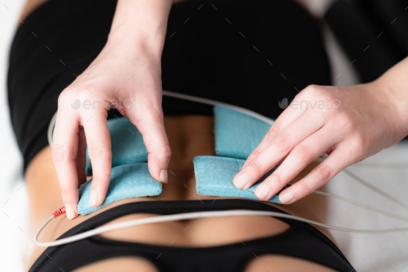 Therapist positioning electrodes onto a female athlete\'s lower back muscles