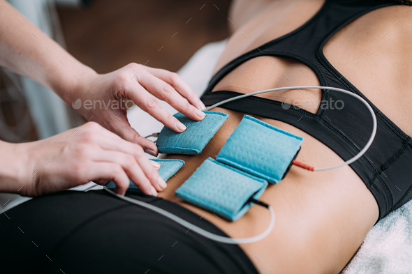 Therapist positioning electrodes onto a female athlete's lower back muscles