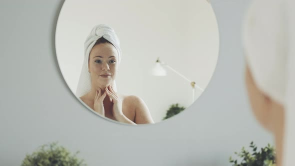 lady after taking shower applies moisturizer to her face and massages skin.