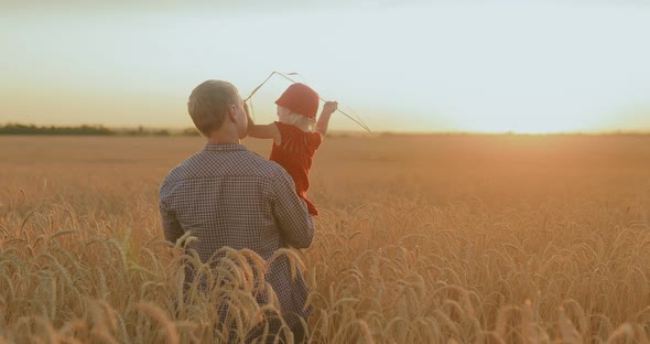 Man with a Baby is Walking on a Wheat Field