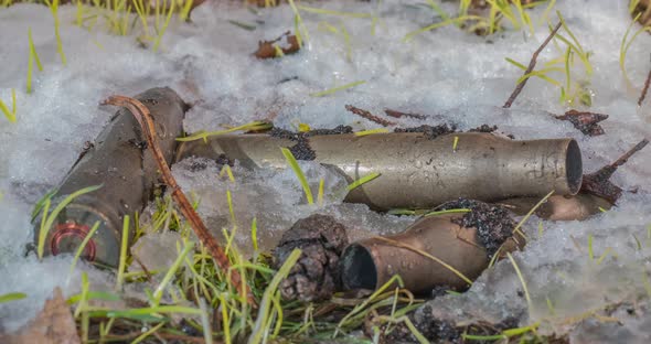 Macro Timelapse Shot of Shiny Melting Snow Particles and Unveiling Green Grass and Machine Gun Ammo alt