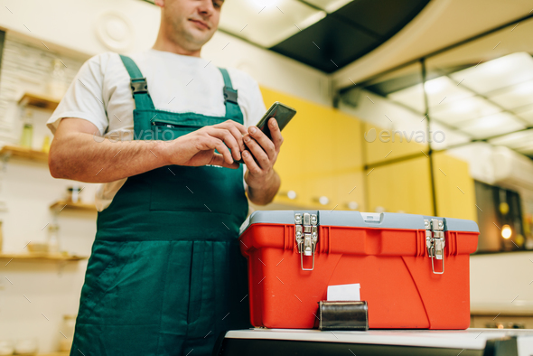 Repairman in uniform holds phone against toolbox - Stock Photo - Images