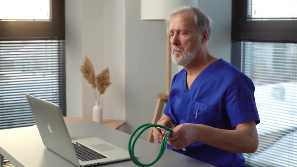 Tired Mature Male Doctor Sitting Down at Table Starting Working Typing on Laptop Computer alt