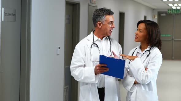 Doctors having discussion over clipboard in corridor alt