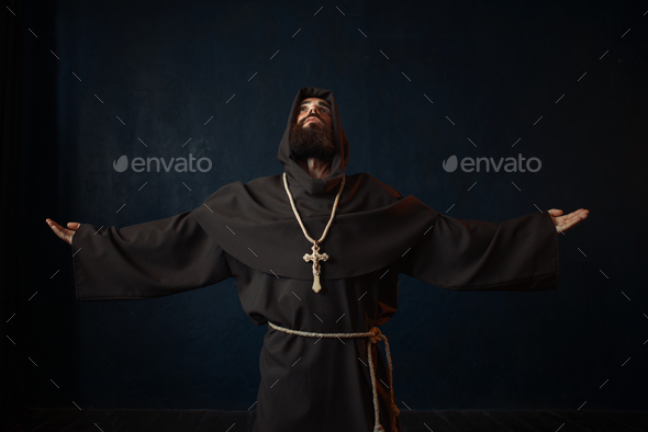 Monk in black robe with hood kneeling and praying - Stock Photo - Images