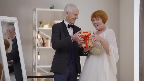 Loving Handsome Senior Groom Giving Gift Box to Excited Bride in Slow Motion alt
