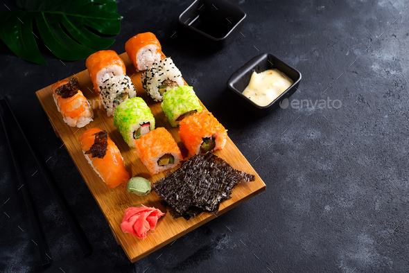 Asian food background with black iron teapot and sushi set on wooden plate on black stone table