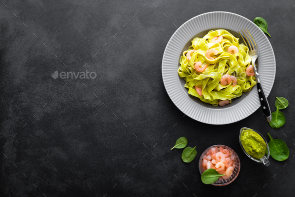 Boiled fettuccine pasta with fresh spinach pesto and shrimps on black background. Italian cuisine - Stock Photo - Images
