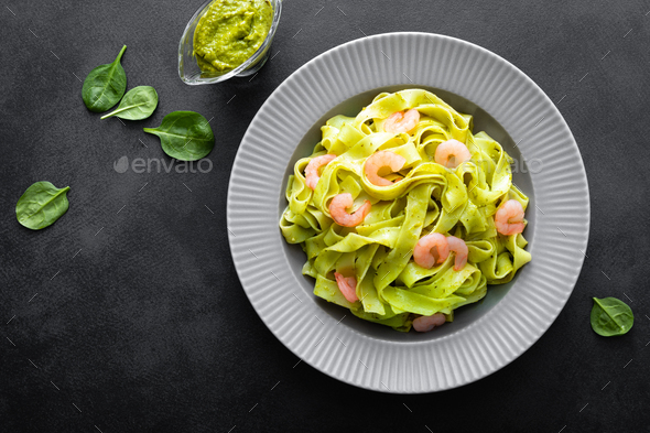 Boiled fettuccine pasta with fresh spinach pesto and shrimps on black background. Italian cuisine - Stock Photo - Images