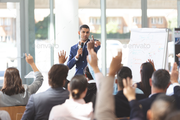 Young businessman speaking at business seminar with diverse group of people raising their hand - Stock Photo - Images