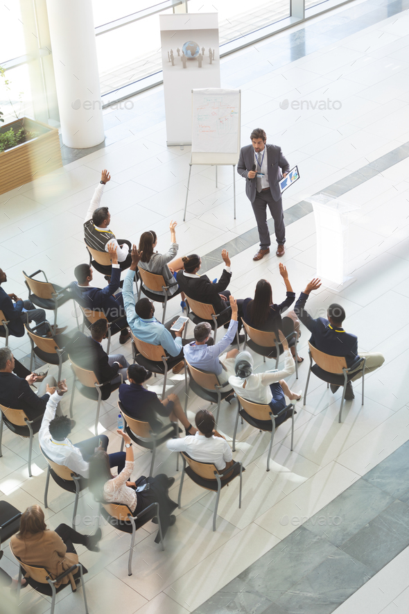 Group of diverse business people raising their hands to ask questions to businessman at conference - Stock Photo - Images