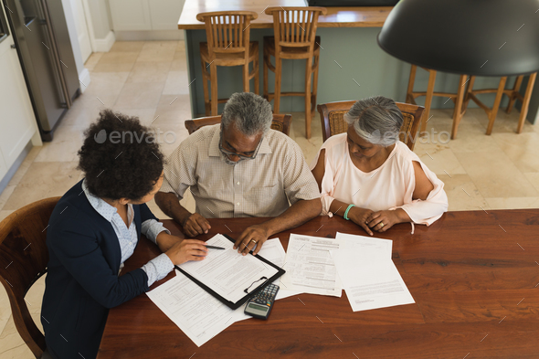 Female real estate agent and a senior couple discussing over documents at the table  - Stock Photo - Images