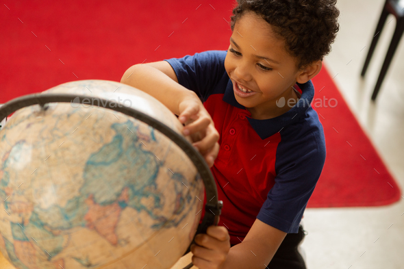 playful schoolboy studying globe at desk in a classroom at elementary school - Stock Photo - Images