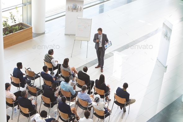 Man speaker with digital tablet speaks in a business seminar in front of diverse business people - Stock Photo - Images