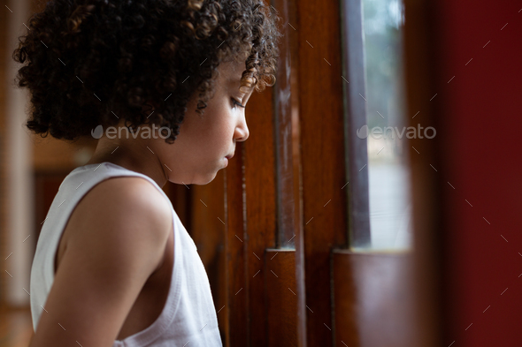Side view of a mixed-race schoolboy looking through window in basketball court at school