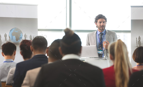 Businessman speaking in front of diverse group of business executives at business seminar in office