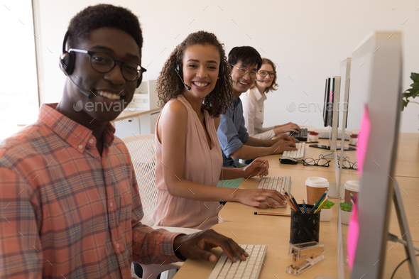 Young diverse executives working on personal computer while communicating on headset in office