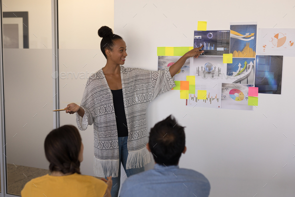 Female executive explaining graphs and sticky notes to diverse business team in modern office