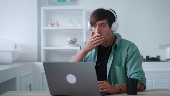 Scared Young Man in Headphones Getting Bad Results on Computer at Home Office alt