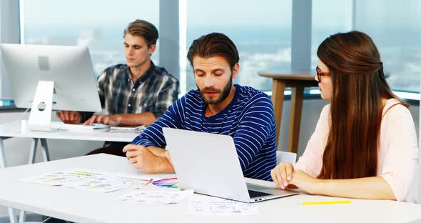 Graphic designers discussing over laptop at desk alt