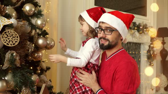 Father with Child Girl Decorate Christmas Tree on Background of Fireplace