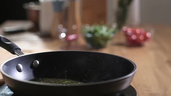 Cook pours olive oil into preheated frying pan and tosses frozen green beans alt