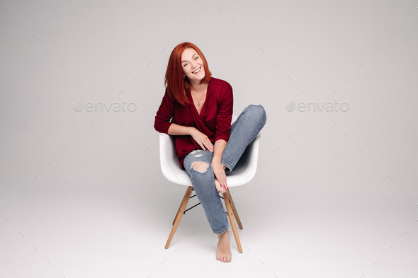 Model with ginger hair sitting on white chair in studio - Stock Photo - Images