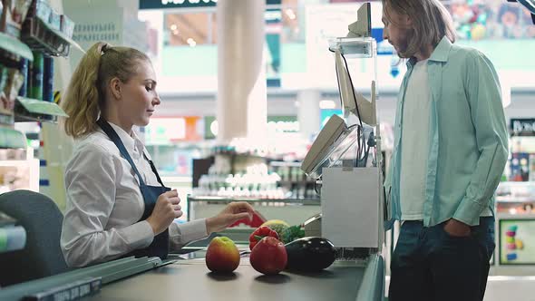 Female Cashier at Work in an Organic Store Man is Pays at the Checkout of the Grocery Store with Nfc alt