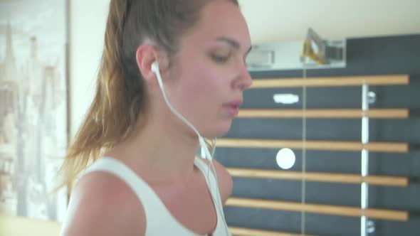 Young woman running on treadmill in headphones. Slow motion  alt