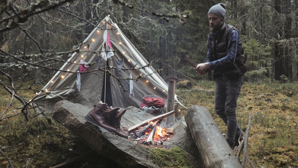 Adventurer Chopping Wood With Axe by the Campfire and Vintage Tent alt